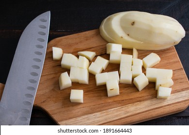 Dicing A Peeled Russet Potato: Chopping A Raw Potato On A Wooden Cutting Board