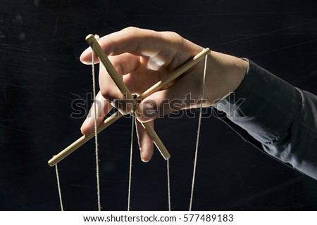Dictator's arm holds  strings for manipulation on black background.