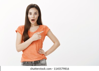 Did You Heard What She Said. Studio Shot Of Amazed And Stunned Caucasian Female, Dropping Jaw And Expressing Surprise With Shock While Pointing At Upper Right Corner Over Gray Background