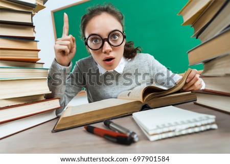 Did you know that?! Curious student reads a books. Photo of astonished young girl wearing glasses pointing finger up. Education concept