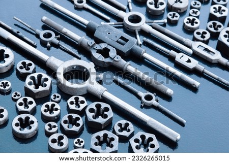 A lot of dies and holders for them of different sizes for threading in metal, on a black background.