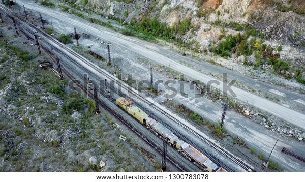 Diesel\
locomotive is pushing dump-car filled with rubble stone in the\
background of a quarry for limestone\
mining