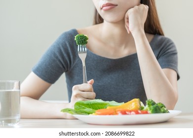 Diet in bored, unhappy beautiful asian young woman, girl on dieting, holding fork at broccoli in salad plate, dislike or tired with eat fresh vegetables. Nutrition of clean, healthy food good taste.