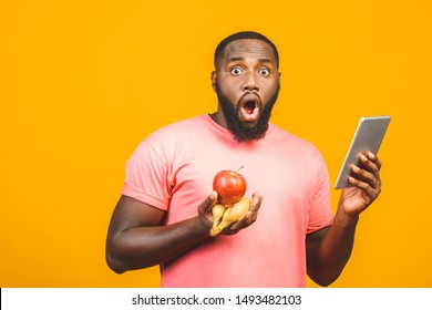 Diet concept. Healthy african american black man holding fruits isolated against yellow background. Using tablet fo searching recipe. 