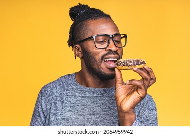 Diet concept. Hungry african american black bearded man eating donut isolated over yellow background. Junk food.