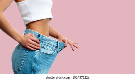 Diet concept and weight loss. Woman in oversize jeans on pastel pink background