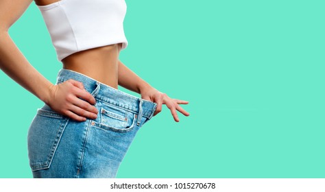 Diet concept and weight loss. Woman in oversize jeans on pastel green background - Shutterstock ID 1015270678