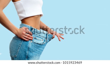 Diet concept and weight loss. Woman in oversize jeans on pastel blue background