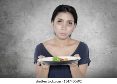 Diet concept. Young woman looks unhealthy while holding a plate of small portion salad