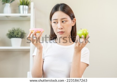Diet, Dieting asian young woman or girl smile, confused choose, choice green apple or pink sweet donut, at home, eat food for good healthy, health when hungry. Close up female weight loss person.