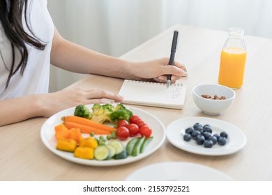 Diet, Dieting hand of woman write diet plan right nutrition on table with fresh vegetables salad, almond is different food ingredients in the green. Nutritionist of healthy, nutrition of weight loss.