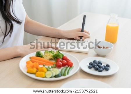 Diet, Dieting hand of woman write diet plan right nutrition on table with fresh vegetables salad, almond is different food ingredients in the green. Nutritionist of healthy, nutrition of weight loss.