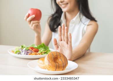 Diet, dieting, happy asian young woman, girl hand push out, deny sweet donut, doughnut on plate, choose red apple and green vegetable salad, eat food for good healthy, female getting weight loss. - Shutterstock ID 2333485347