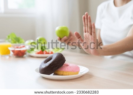 Diet, dieting, happy asian young woman, girl hand push out, deny sweet donut or dessert doughnut on plate, choose green apple and vegetable salad, eat food for good healthy, female getting weight loss