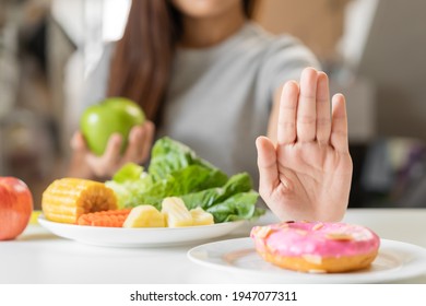 Diet, Dieting young asian woman or girl use hand push out, deny sweet donut and choose green apple, vegetables salad, eat food for good healthy, health when hungry. Close up female weight loss person. - Shutterstock ID 1947077311
