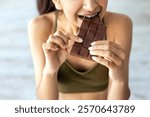 Diet failure, cheat meal and unhealthy nutrition concept. Above view of Indian woman eating chocolate while standing on scales, closeup. Hungry Hindu lady losing control, eating junk food