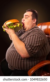 Diet Failure Of Fat Man Eating Fast Food Hamberger. Happy Smile Overweight Person Who Spoiled Healthy Food By Eating Huge Hamburger On Fork. Man Struggles With Hunger For All His Strength.