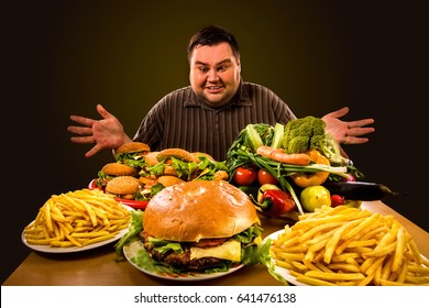 Diet fat man who makes choice between healthy and unhealthy food. Overweight male with hamburgers, french fries and vegetables trays trying to lose weight first time Dinner is field of the working day