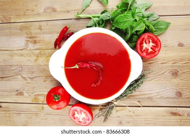 diet food : hot tomato vegetable soup with basil thyme and raw tomatoes in white round bowl over red mat on wood table ready to eat