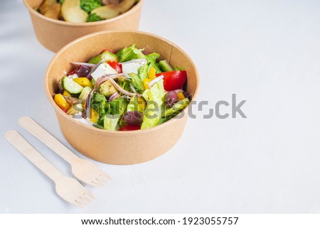 Diet Greek salad with feta, tomatoes, greens on light background top view. Healthy lunch. Food delivery in disposable plate of craft paper. Eco-friendly carton packaging environment protection