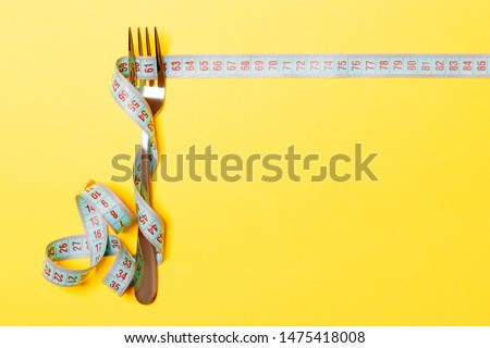 Diet and healthy eating concept with fork and measuring tape on yellow background. Top view of weightloss.