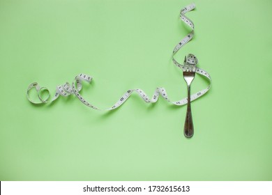 Diet and healthy eating concept. Top view of weightloss. Measuring tape on a fork. Green background - Shutterstock ID 1732615613