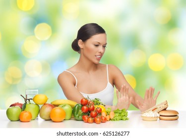 Diet, Healthy Eating, Food And People - Woman With Fruits And Vegetables Rejecting Hamburger And Sandwich On Table Over Green Summer Lights Background