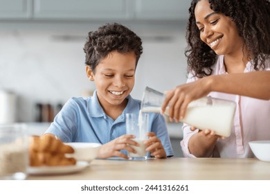 Diet for kids. Loving african american mother pouring fresh milk for her son. Happy preteen black child enjoying healthy nutritive breakfast with his mom, kitchen interior, copy space - Powered by Shutterstock