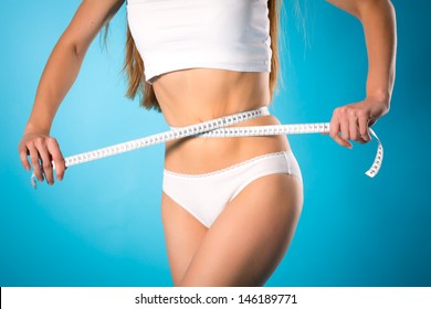 Diet and loosing weight - young woman is measuring her waist with measuring tape