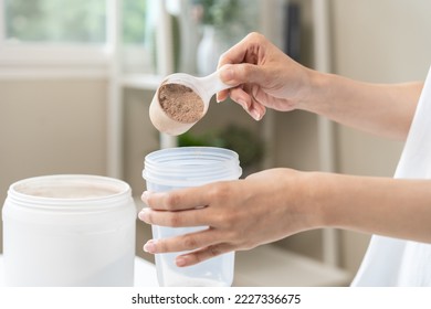 Diet meal replacement for weight loss, asian young woman in sportswear, hand in holding scoop making protein into bottle to shake, drink supplement for muscle after workout at home. Healthy body care. - Shutterstock ID 2227336675