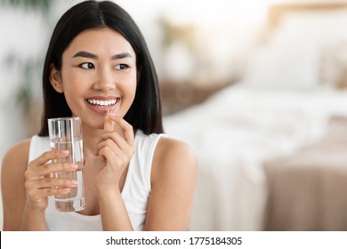 Diet, Nutrition, Healthy Eating Concept. Close Up Of Happy Smiling Asian Woman Taking Supplement Pill And Holding Glass Of Fresh Water In Morning, Copy Space