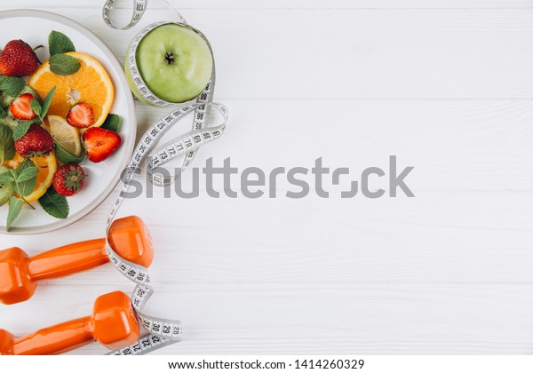 Diet plan, menu or program, tape measure, water,\
dumbbells and diet food of fresh fruits on white background, weight\
loss and detox concept, top\
view