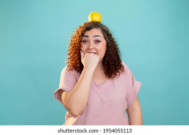 Diet Struggle. Plus Size Woman. Healthy Food. Overweight Problem. Body Shaming. Conceptual Portrait. Pretty Fatty Lady Biting Hand Fists Apple On Head Isolated Blue.