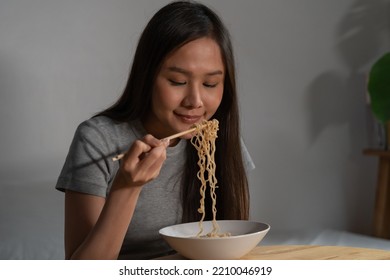 Diet, Templtation. Alone Asian Young Student Woman, Girl Using Chopsticks Eating Instant Ramen, Noodles In Bowl On Table In Bedroom In Overtime Night, Late Time At Home.