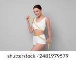 Diet and weight loss concept. Beautiful young woman with measuring tape showing her slim body against light grey background