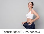 Diet and weight loss concept. Happy young woman in big jeans showing her slim body on light grey background. Space for text