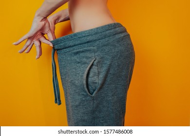 Diet And Weight Loss Theme On The Orange Background. Woman Lost Weight. Clothes Is Too Big. Thin Woman On Diet Before And After.