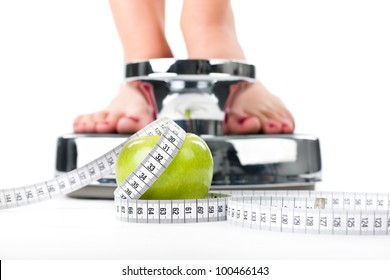 Diet and weight, young woman standing on a scale, only feet to be seen, a apple and a measuring tape