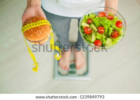 Diet. Woman Measuring Body Weight On Weighing Scale Holding Burger and Salad. Sweets Are Unhealthy Junk Food. Dieting, Healthy Eating, Lifestyle. Weight Loss. Obesity. Top View.
