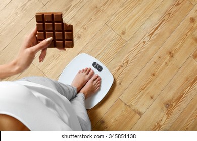 Diet. Young Woman Standing On Weighing Scale And Holding Chocolate Bar. Sweets Are Unhealthy Junk Food. Sugar Is Bad For Health. Dieting, Healthy Eating, Lifestyle. Weight Loss. Top View