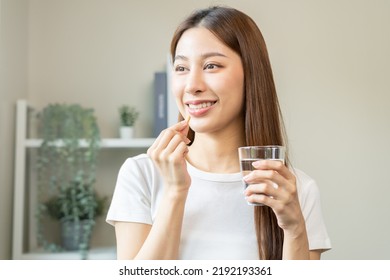 Dietary supplement, asian young woman, girl hand holding orange medical pill, take or eat vitamin C, D for treatment for skin, hair and nail strengthen with glass of pure water at home, healthcare. - Shutterstock ID 2192193361