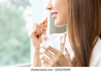 Dietary supplement, asian young woman, girl hand holding orange medical pill, take or eat vitamin C, D for treatment for skin, hair and nail strengthen with glass of pure water at home, healthcare. - Shutterstock ID 2201070949