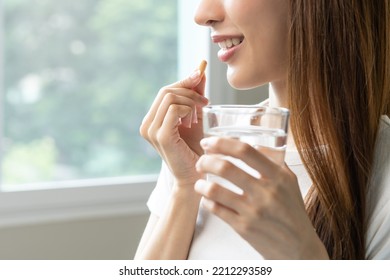Dietary supplement, asian young woman, girl hand holding orange medical pill, take or eat vitamin C, D for treatment for skin, hair and nail strengthen with glass of pure water at home, healthcare. - Shutterstock ID 2212293589