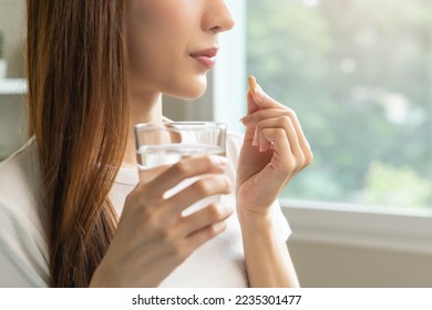 Dietary supplement, asian young woman, girl hand holding orange medical pill, take or eat vitamin C, D for treatment for skin, hair and nail strengthen with glass of pure water at home, healthcare. - Shutterstock ID 2235301477