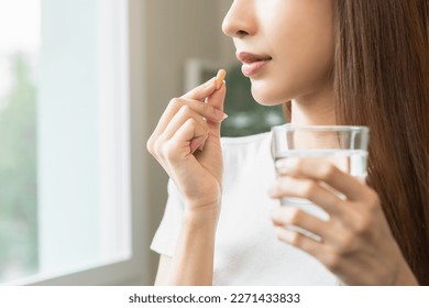 Dietary supplement, asian young woman, girl hand holding orange medical pill, take or eat vitamin C, D for treatment for skin, hair and nail strengthen with glass of pure water at home, healthcare. - Shutterstock ID 2271433833