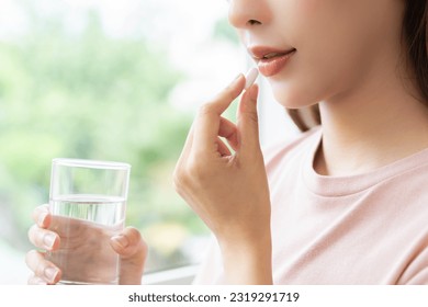 Dietary supplement asian young woman hand holding medical pill capsule, take or eat vitamin in mouth for treatment, sick female taking medicines drinking with water at home, pharmacy and healthcare. - Shutterstock ID 2319291719