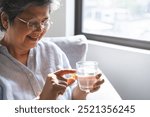 Dietary supplement health care concept, happy smile asian senior woman hand holding fish oil pills, drug tablet, take medicine with glass of water, aged take vitamin for treatment body strong at home.