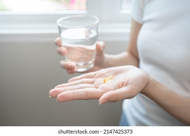 Dietary Supplement, Nutrition asian woman, young hand in holding yellow pill, talking daily vitamin D, E, A, fish oil pill for hair and skin with glass of water. Diet healthy eating, beauty people.