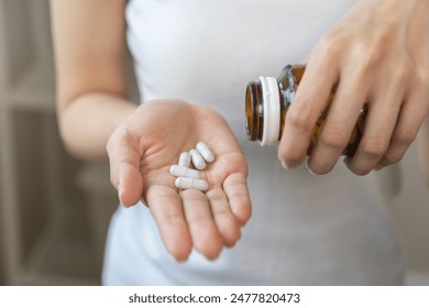 Dietary supplement or sick, asian young woman, girl hold pills, drugs medical tablet on hand pouring capsules from medication bottle, take vitamin for treatment for skin, hair at home, healthcare.