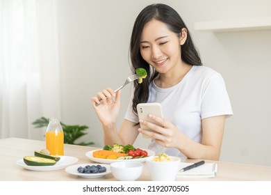 Dieting, asian young woman eating, holding fork at broccoli, diet plan nutrition with fresh vegetables salad, enjoy meal while using smartphone. Nutritionist of healthy, nutrition of weight loss. - Powered by Shutterstock